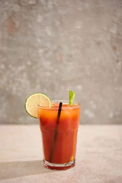 Bloody mary cocktail in glass with lime, celery and straw on grey background — Stock Photo