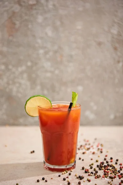 Bloody mary cocktail in glass with lime, celery and straw on grey background with black pepper — Stock Photo