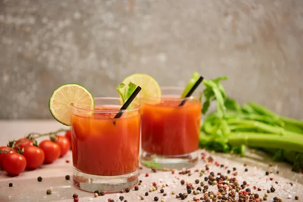 Cocktail Mary sanglant dans des verres avec des pailles et du citron vert près de sel, poivre, tomates et céleri sur fond gris — Photo de stock