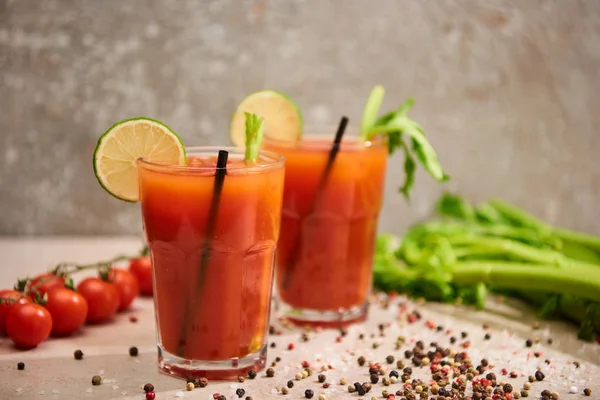 Bloody mary cocktail in glasses with straws and lime near salt, pepper, tomatoes and celery on grey background — Stock Photo