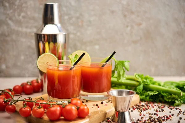 Cocktail mariano insanguinato in bicchieri con paglie e lime su asse di legno vicino a sale, pepe, pomodori e sedano — Foto stock