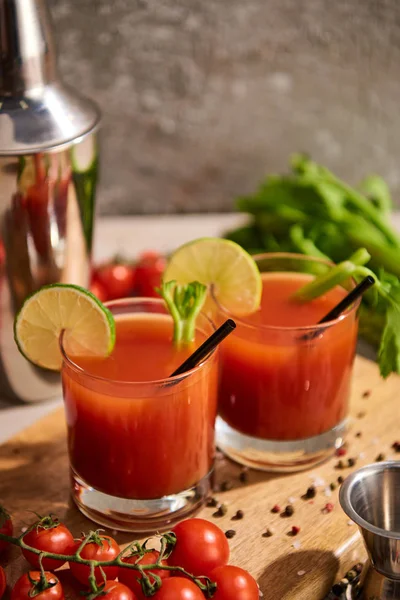 Foyer sélectif de cocktail Mary sanglant dans des verres sur planche de bois près de sel, poivre, tranches de citron vert, tomates et céleri — Photo de stock