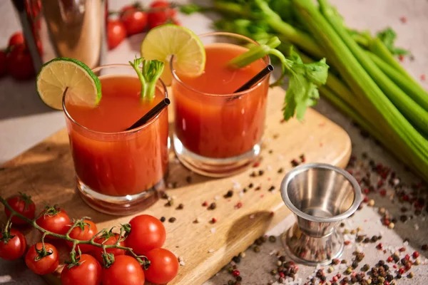 Cocktail marie sanglant dans des verres sur planche de bois près de sel, poivre, tranches de citron vert, tomates et céleri — Photo de stock