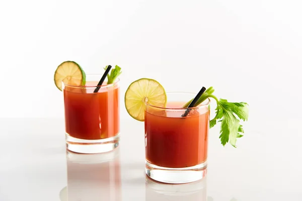 Bloody mary cocktail in glasses garnished with lime and celery isolated on white — Stock Photo