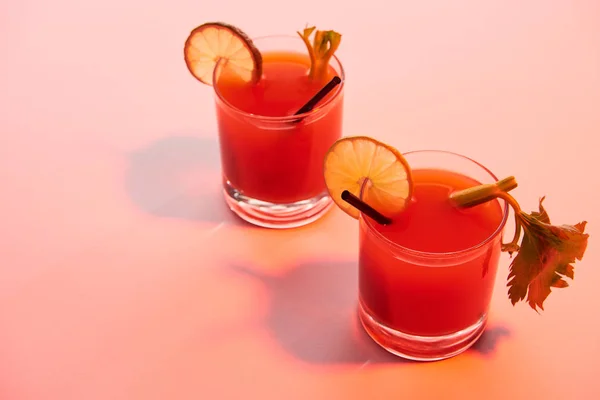 Bloody mary cocktail in glasses garnished with lime and celery on red illuminated background — Stock Photo