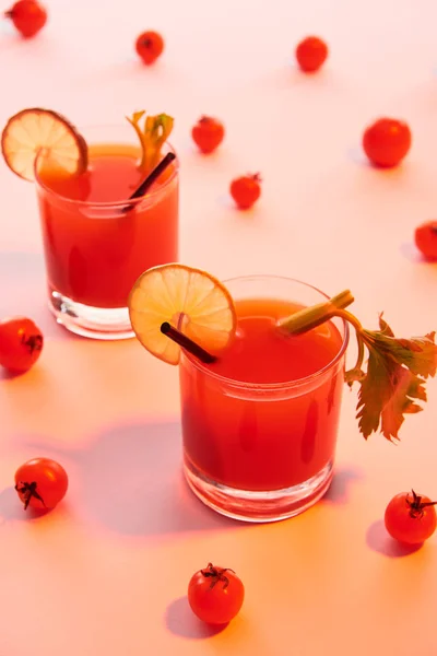 Bloody mary cocktail in glasses garnished with lime and celery on red illuminated background with tomatoes — Stock Photo