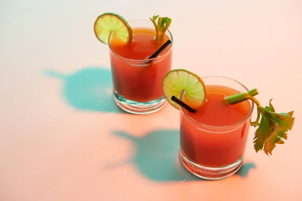 Bloody mary cocktail in glasses garnished with lime and celery on red and blue illuminated background — Stock Photo