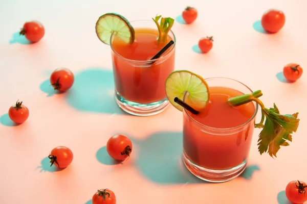 Bloody mary cocktail in glasses garnished with lime and celery on illuminated background with tomatoes — Stock Photo