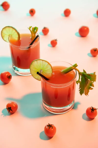 Selektiver Fokus des blutigen Mary-Cocktails in Gläsern mit Limette und Sellerie auf beleuchtetem Hintergrund mit Tomaten — Stockfoto