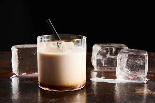 White russian cocktail in glass near melting ice cubes isolated on black — Stock Photo