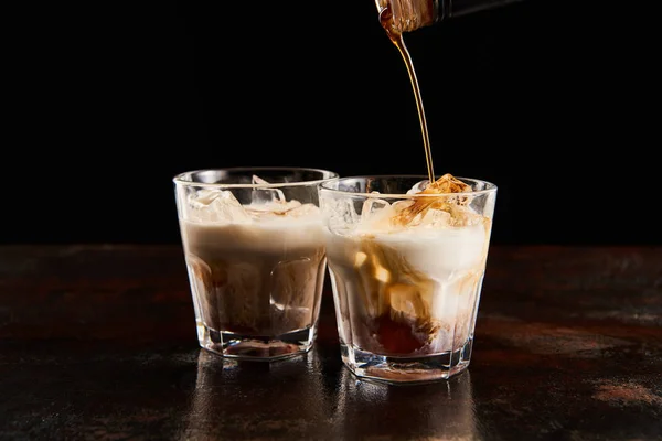 Coffee liquor poring in glasses with ice cubes isolated on black — Stock Photo