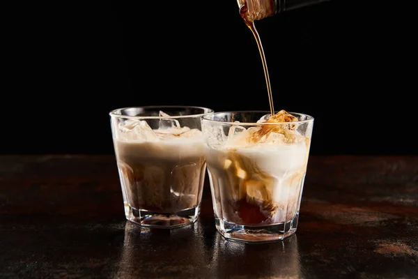 Licor de café poring em copos com cubos de gelo isolados em preto — Fotografia de Stock