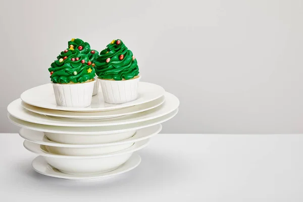 Deliziosi cupcake dell'albero di Natale con piatti su superficie bianca isolati su grigio — Foto stock