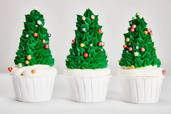 Deliciosos cupcakes de árbol de Navidad en fila en la superficie blanca aislado en gris - foto de stock