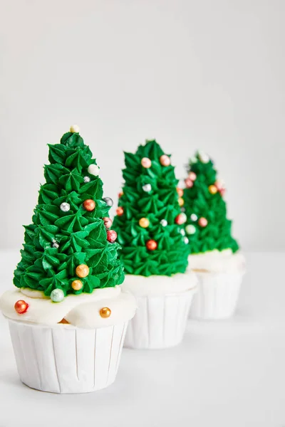 Foco selectivo de deliciosos cupcakes de árbol de Navidad en fila en la superficie blanca aislado en gris - foto de stock