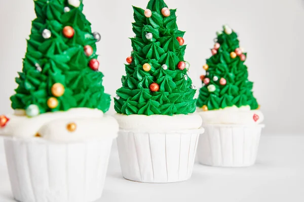 Selective focus of delicious Christmas tree cupcakes in row on white surface isolated on grey — Stock Photo