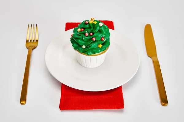 Delizioso cupcake su piatto bianco con posate dorate e tovagliolo rosso su superficie bianca — Foto stock