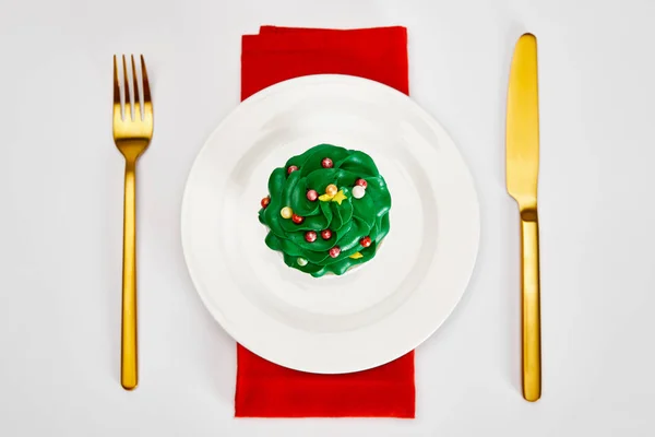 Вид сверху на вкусный кекс на белой тарелке с золотыми столовыми приборами и красной салфеткой на белой поверхности — стоковое фото
