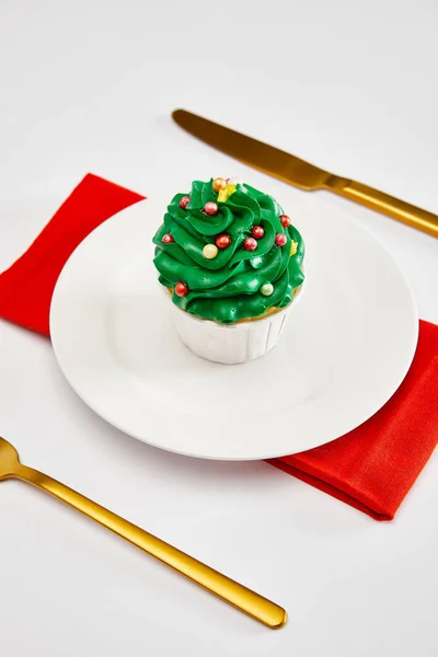 Delicioso cupcake en plato blanco con cubiertos de oro y servilleta roja en la superficie blanca - foto de stock