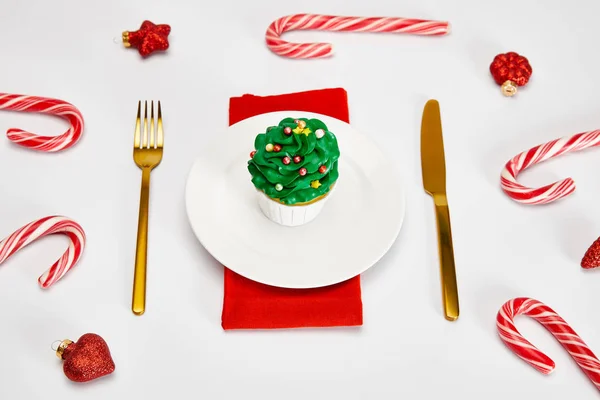 Вкусный кекс на белой тарелке с золотыми столовыми приборами, конфеты, безделушки и красной салфеткой на белой поверхности — стоковое фото
