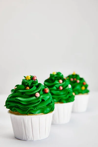 Selektiver Fokus von leckeren Weihnachtsbaum-Cupcakes in Reihe auf weißer Oberfläche isoliert auf grau — Stockfoto