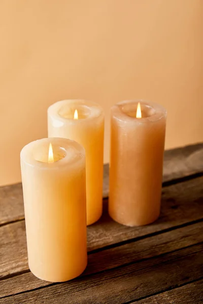 Drei brennende Kerzen auf Holztisch auf beige — Stockfoto