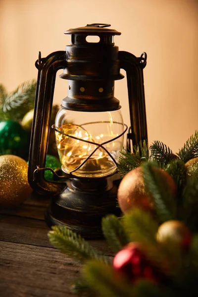 Decorative vintage oil lamp with lights, spruce branches and christmas balls on beige — Stock Photo