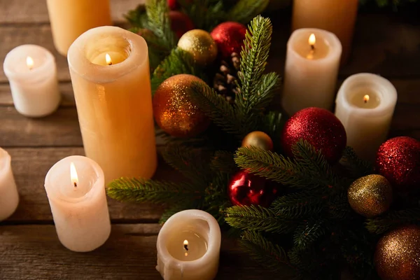Burning candles with spruce wreath, red and golden christmas balls on wooden table — Stock Photo