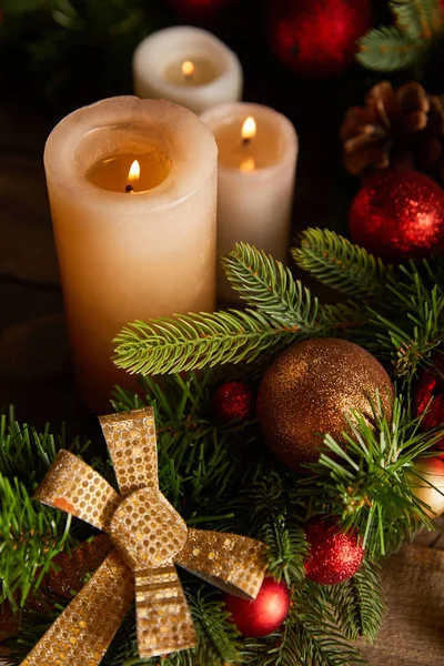 Nahaufnahme brennender Kerzen mit Fichtenzweigen, Bogen und Weihnachtskugeln auf Holztisch — Stockfoto