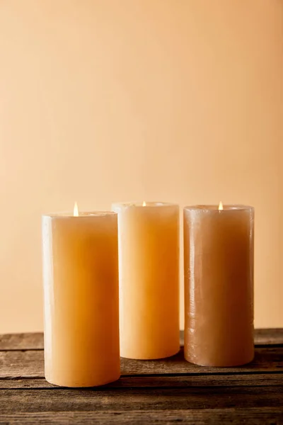 Three festive burning candles on wooden table on beige — Stock Photo