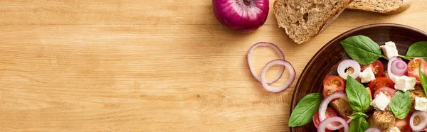 Vista dall'alto di deliziosa insalata di verdure italiana panzanella servita su piatto su tavola di legno vicino a ingredienti freschi, colpo panoramico — Foto stock