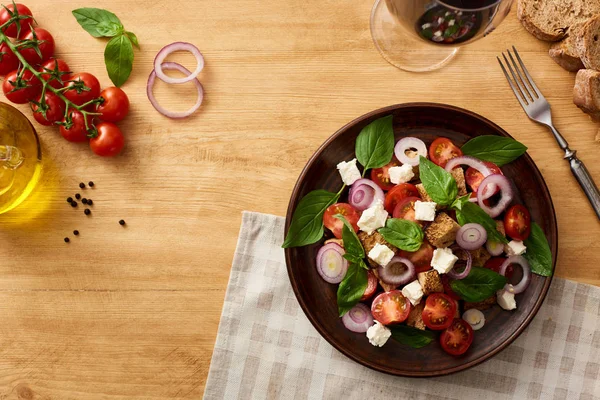 Vista superior da deliciosa salada de legumes italiana panzanella servida em prato em mesa de madeira perto de ingredientes frescos e vinho tinto — Fotografia de Stock