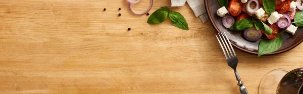 Top view of delicious Italian vegetable salad panzanella served on plate on wooden table near fresh ingredients, fork and red wine, panoramic shot — Stock Photo