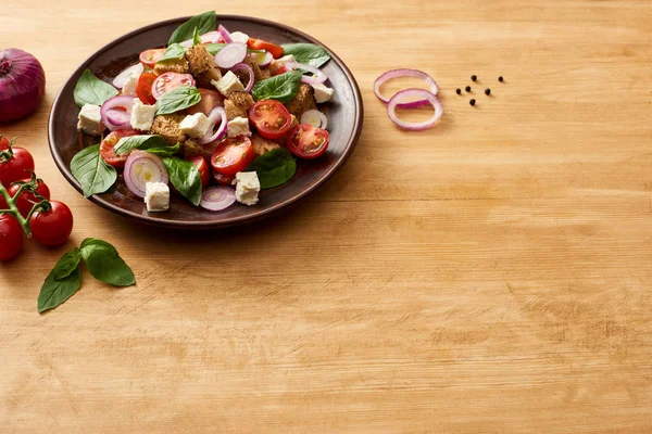 Deliciosa salada de legumes italiana panzanella servida em prato em mesa de madeira perto de ingredientes frescos — Fotografia de Stock