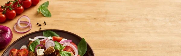 Deliciosa ensalada de verduras italiana panzanella servido en el plato en la mesa de madera cerca de ingredientes frescos, tiro panorámico - foto de stock