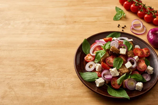 Köstliche italienische Gemüsesalat Panzanella serviert auf Teller auf Holztisch in der Nähe von frischen Zutaten — Stockfoto