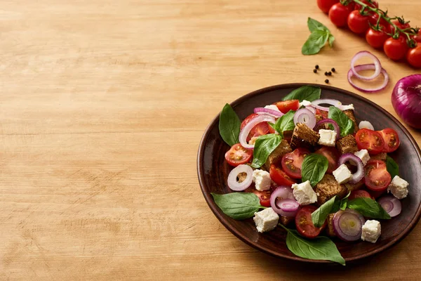 Deliciosa ensalada de verduras italiana panzanella servido en el plato en la mesa de madera cerca de ingredientes frescos - foto de stock