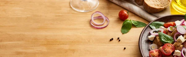 Deliziosa insalata di verdure italiana panzanella servita su piatto su tavola di legno vicino a ingredienti freschi, colpo panoramico — Foto stock