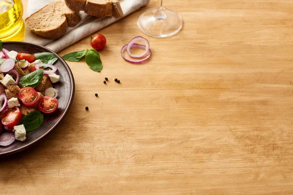 Köstliche italienische Gemüsesalat Panzanella serviert auf Teller auf Holztisch in der Nähe von frischen Zutaten — Stockfoto