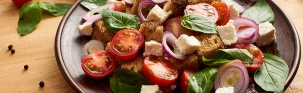 Vista de cerca de la deliciosa ensalada de verduras italiana panzanella servido en el plato en la mesa de madera, plano panorámico - foto de stock