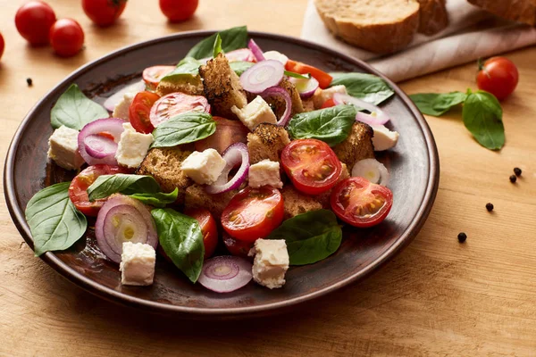 Deliciosa salada de legumes italiana panzanella servida em prato em mesa de madeira perto de ingredientes frescos — Fotografia de Stock
