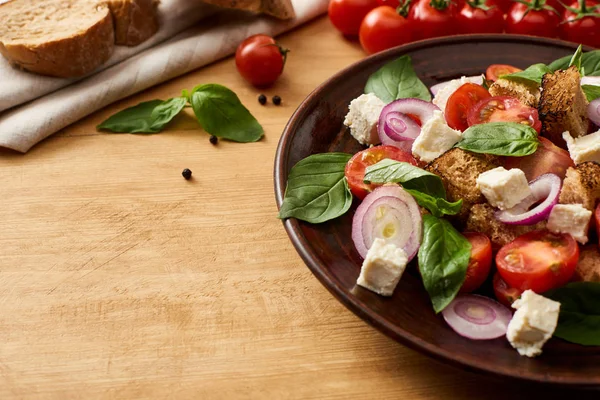 Deliciosa salada de legumes italiana panzanella servida em prato em mesa de madeira perto de ingredientes frescos e pão — Fotografia de Stock