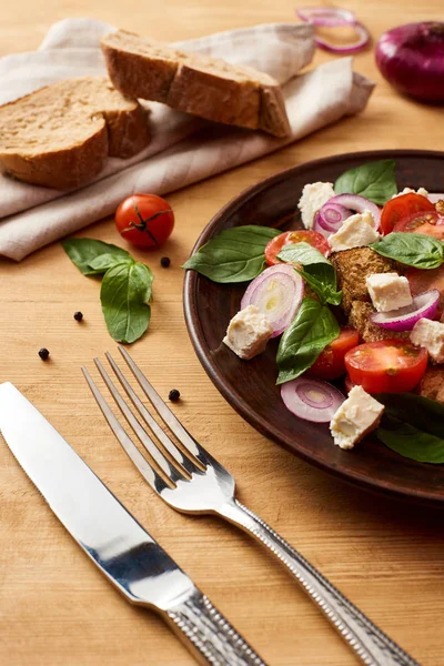 Délicieuse salade de légumes italienne panzanella servie dans une assiette sur une table en bois près de couverts — Photo de stock
