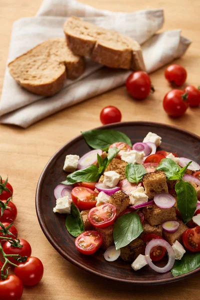 Enfoque selectivo de la deliciosa ensalada de verduras italiana panzanella servido en el plato en la mesa de madera cerca de tomates frescos y pan - foto de stock