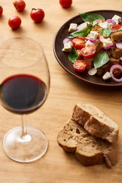 Селективное внимание вкусный итальянский овощной салат panzanella подается на тарелке на деревянный стол рядом с красным вином и хлебом — стоковое фото