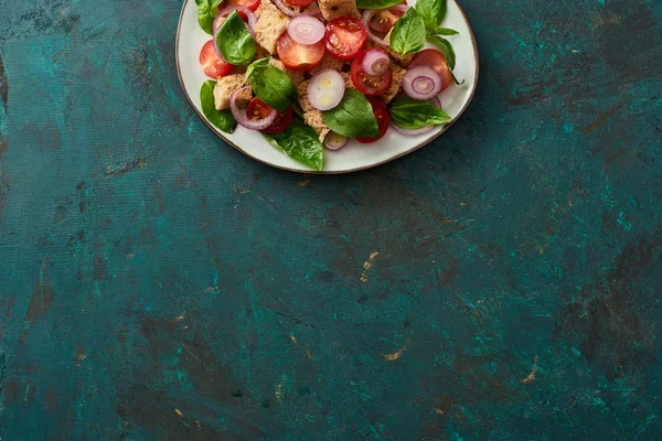 Draufsicht auf köstlichen italienischen Gemüsesalat Panzanella serviert auf Teller auf texturierter grüner Oberfläche — Stockfoto