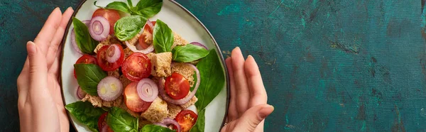 Geschnittene Ansicht einer Frau mit einem Teller mit köstlichem italienischen Gemüsesalat Panzanella auf strukturierter grüner Oberfläche, Panoramaaufnahme — Stockfoto