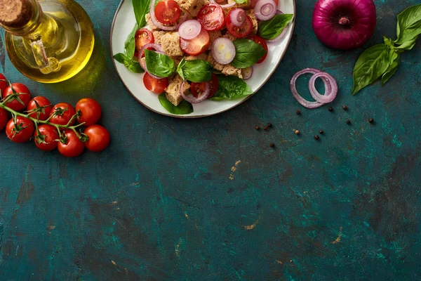 Vista dall'alto della deliziosa insalata di verdure italiana panzanella servita sul piatto su superficie verde strutturata con ingredienti — Foto stock