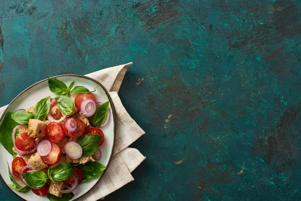 Vue du dessus de délicieuse salade de légumes italienne panzanella servi sur assiette sur surface verte texturée avec serviette — Photo de stock
