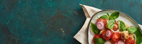 Top view of delicious Italian vegetable salad panzanella served on plate on textured green surface with napkin, panoramic shot — Stock Photo